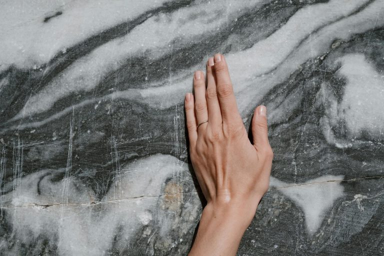 A hand with a ring gently touches a marble surface, highlighting texture and elegance.